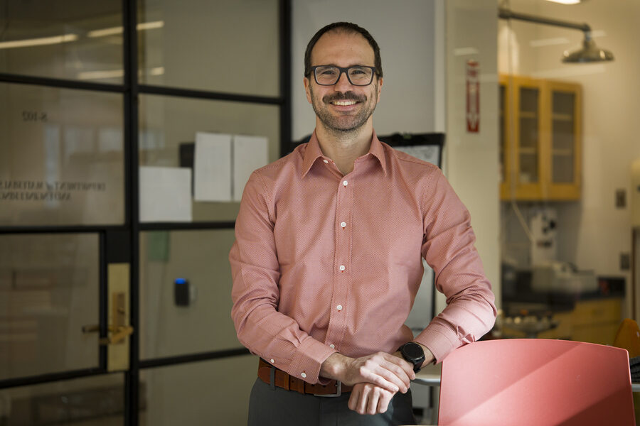 Мужчина в розовой рубашке стоит в офисе рядом с креслом.