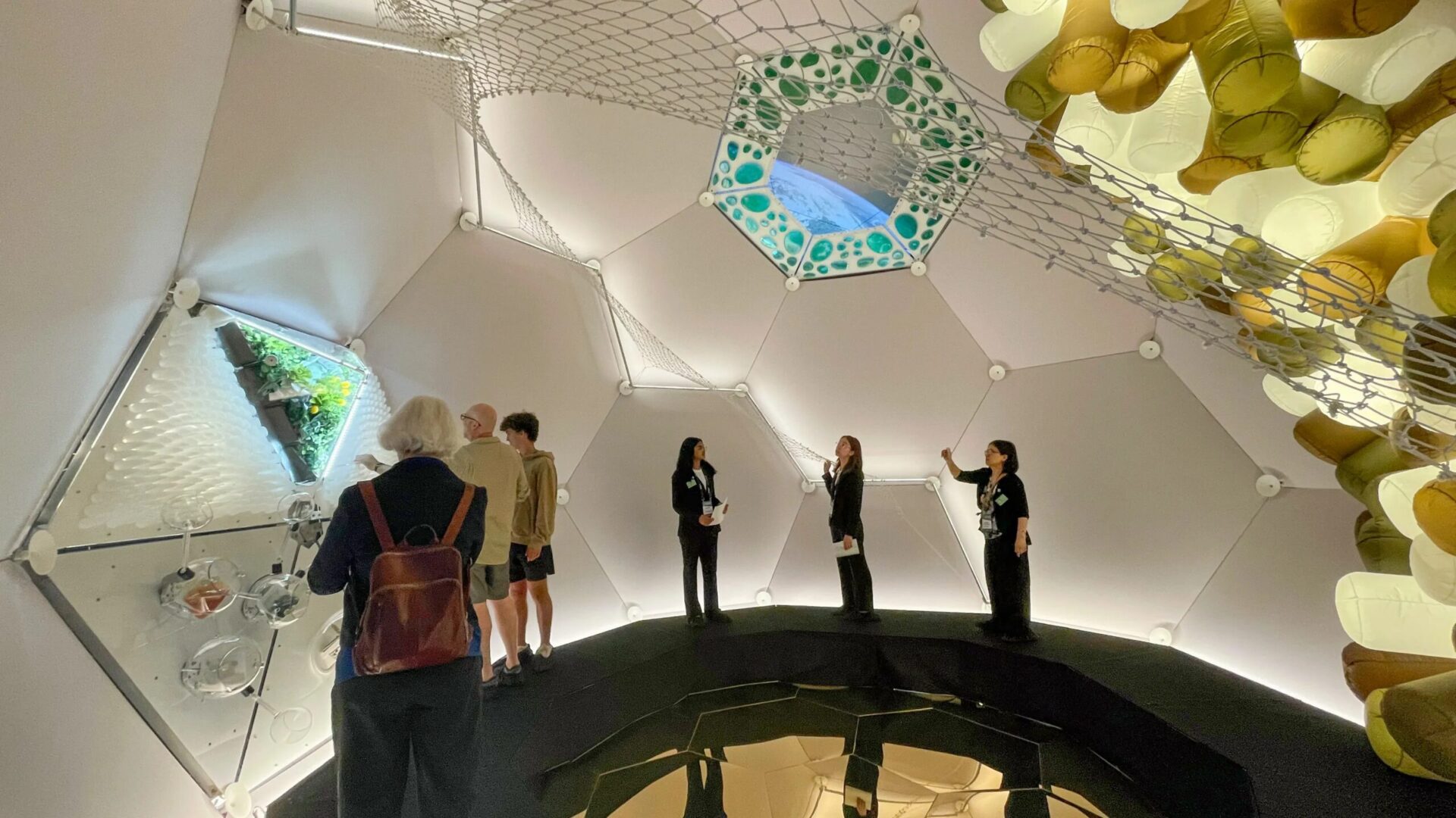 Люди внутри футуристического купола с сеткой, архитектурное пространство с зеркальной поверхностью.