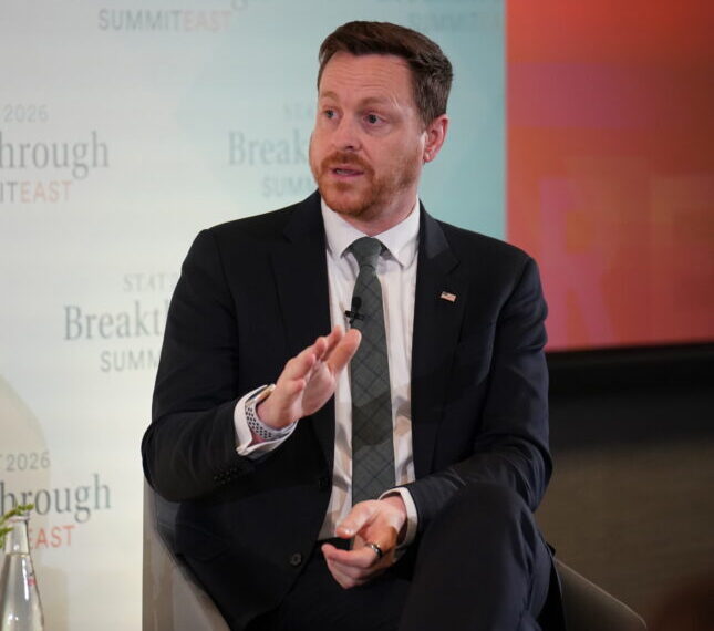 Мужчина в костюме на конференции "Breakthrough Summit East", жест рукой.