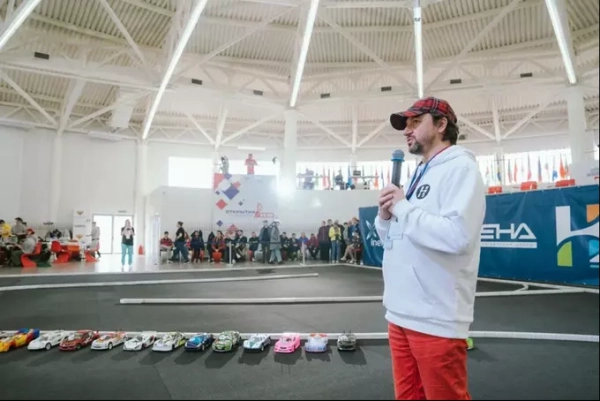 Человек с микрофоном на соревнованиях радиоуправляемых машин в крытом помещении.