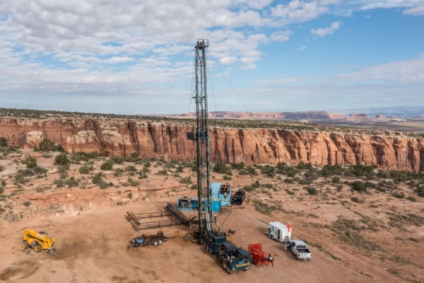 Буровая установка в пустыне на фоне скал и голубого неба.