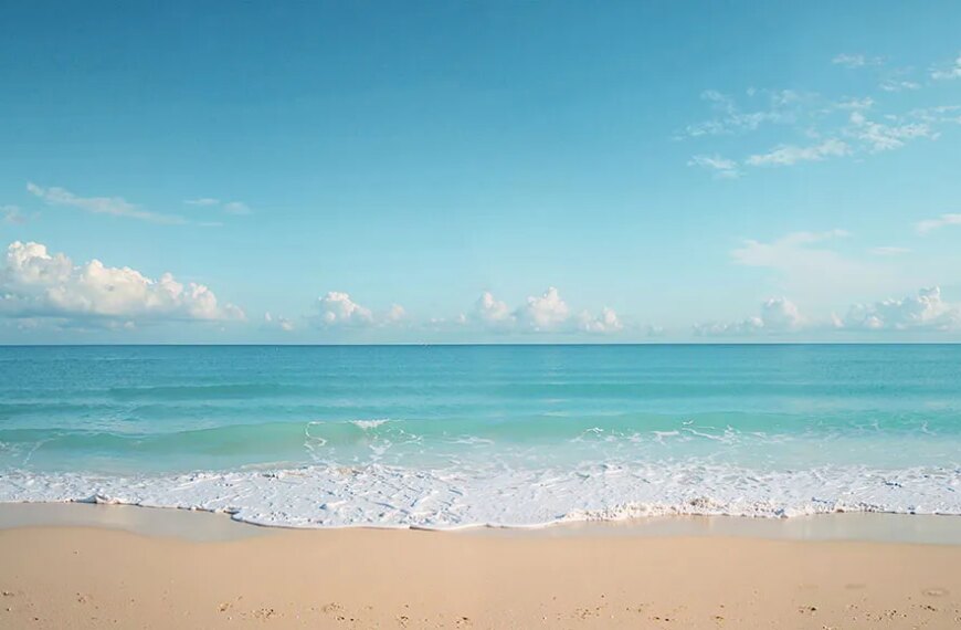 Песчаный пляж и спокойное голубое море с облачным небом на горизонте.