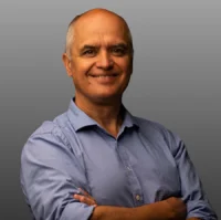 Мужчина в синей рубашке улыбается на сером фоне.