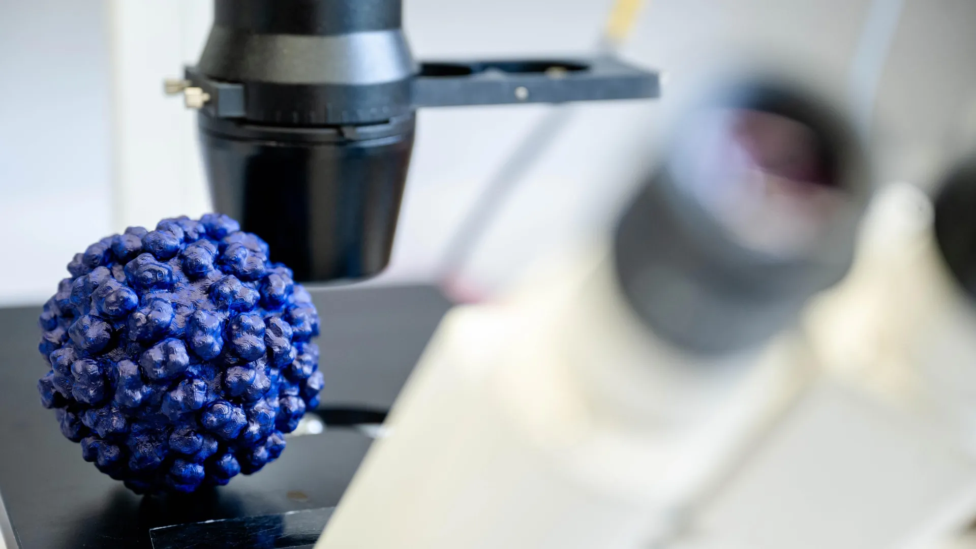 Микроскоп и модель вируса крупным планом на лабораторном столе.