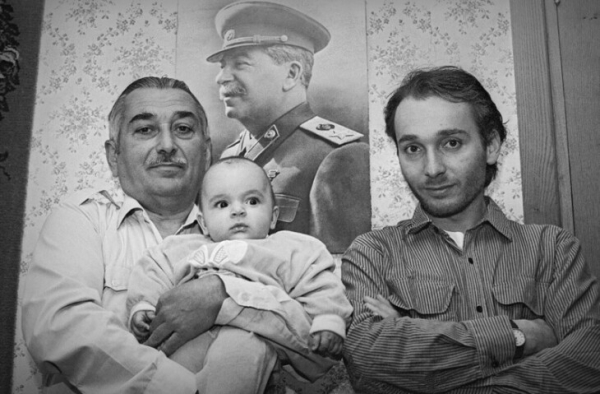 Люди перед портретом военного. Семейный снимок в интерьере. Мужчина держит младенца на руках.