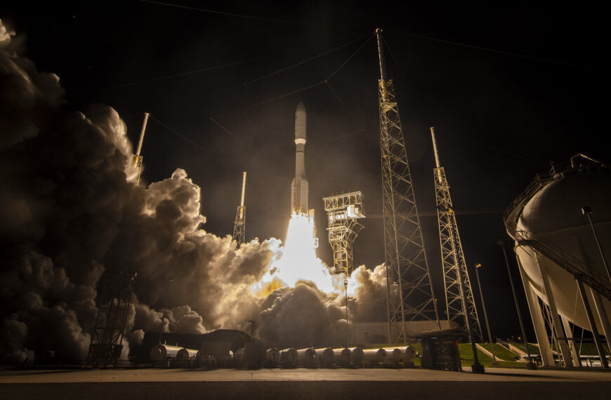 Запуск ракеты в ночи с космодрома, поднимается в небо, окружена дымом.