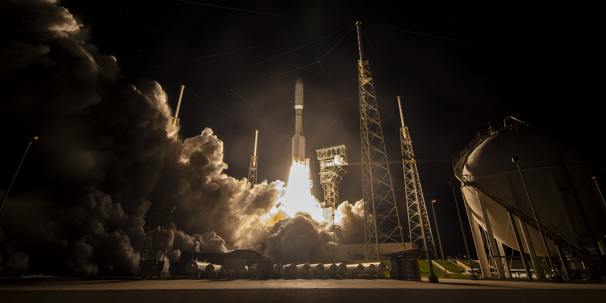 Запуск ракеты в ночи с космодрома, поднимается в небо, окружена дымом.