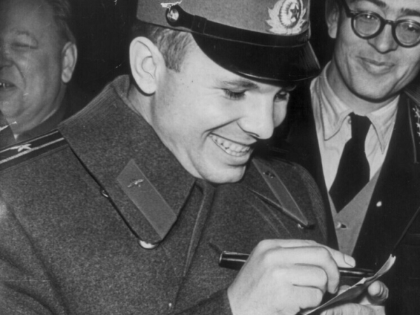 Человек в военной форме улыбается и подписывает документ.