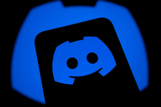 Логотип Discord на экране смартфона, отражающийся на фоне синего цвета.