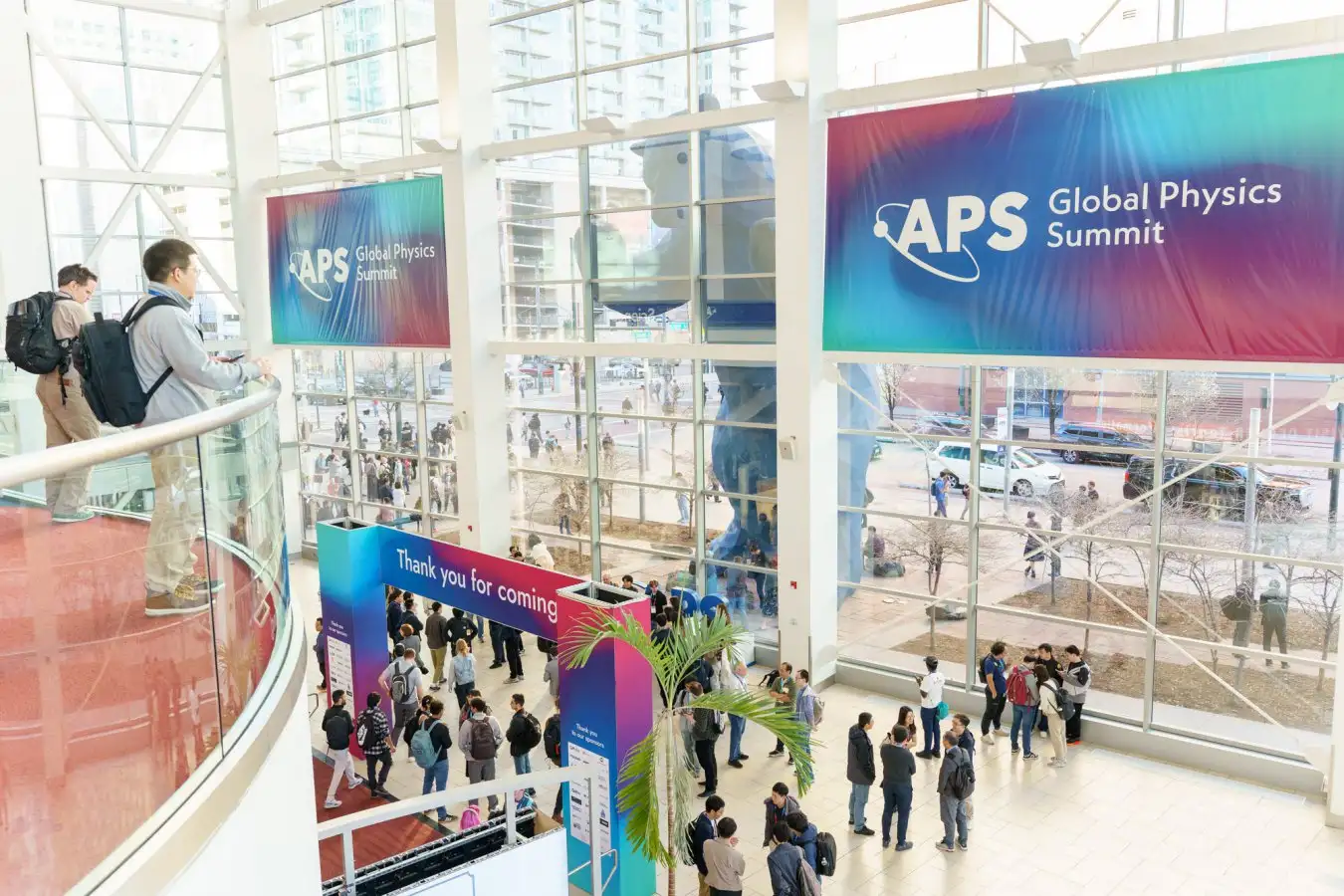 Конференция Global Physics Summit, люди в холле, баннер APS, большое остекление.