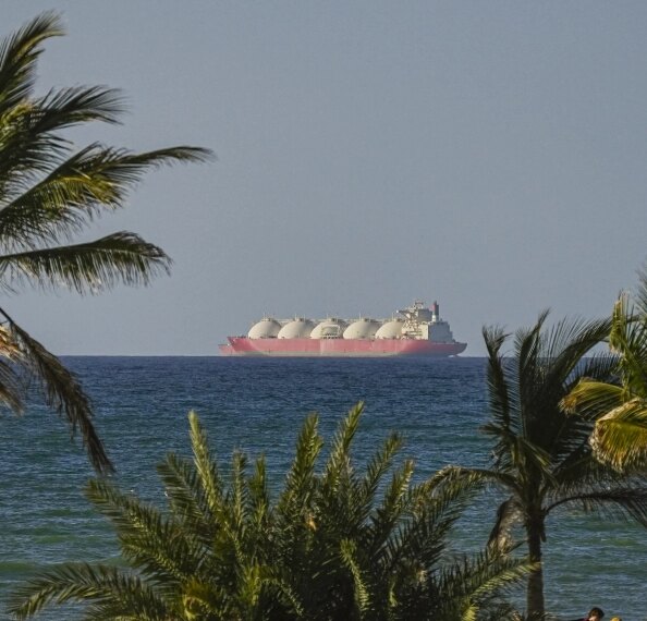 Контейнеровоз с газовыми резервуарами на море среди пальм.