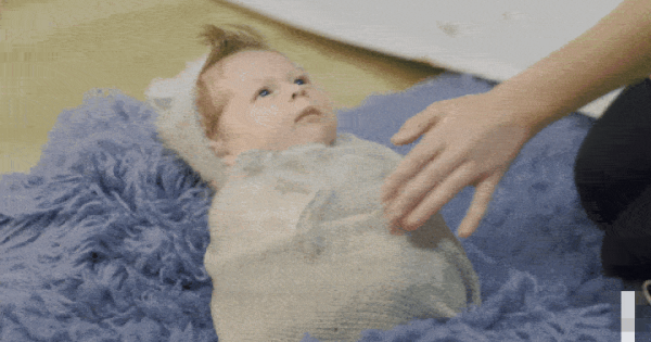 Ребёнок в одеяле лежит на пушистом коврике, рядом рука взрослого.