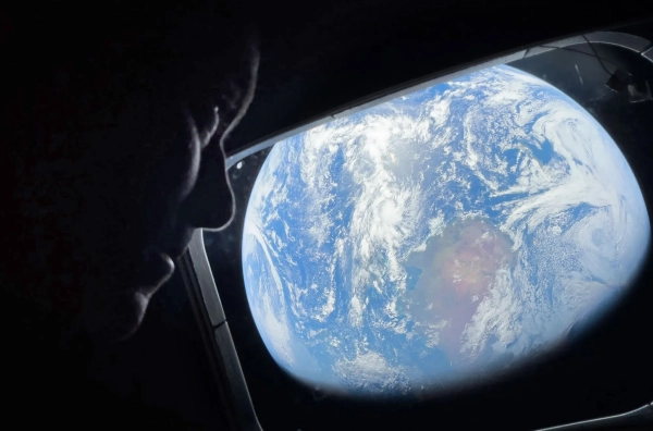 Вид на Землю из космоса через иллюминатор с силуэтом наблюдающего человека.