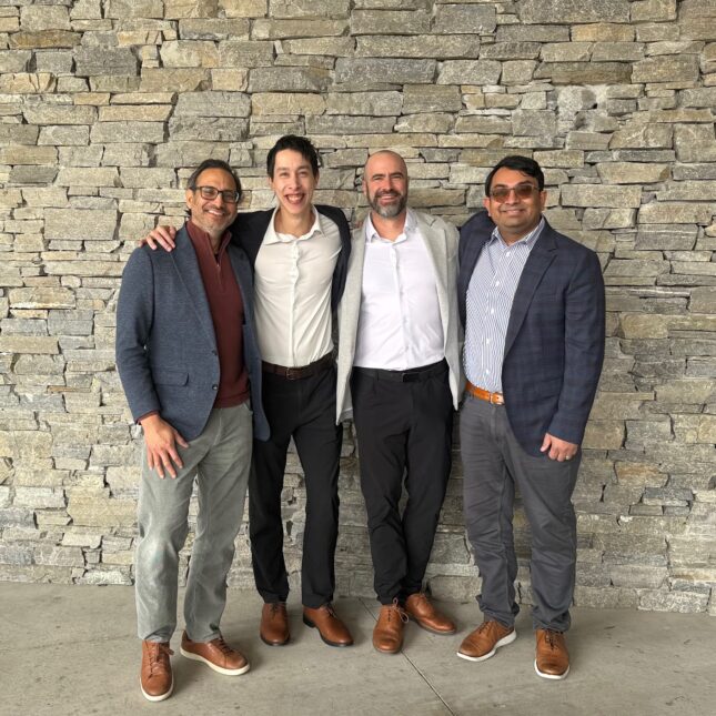 Qualified Health привлекла 125 миллионов долларов для разработки ИИ-решений для медицинских учреждений 1 Четыре мужчины в стильной одежде стоят у каменной стены, дружеская поза.