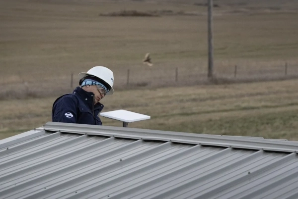 Инженер на крыше с устройством, поле на заднем плане, рабочая экипировка.