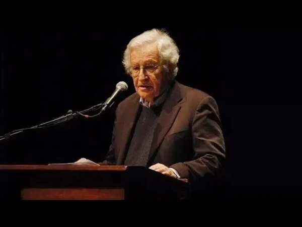 Человек у кафедры выступает с речью, микрофон, темный фон.