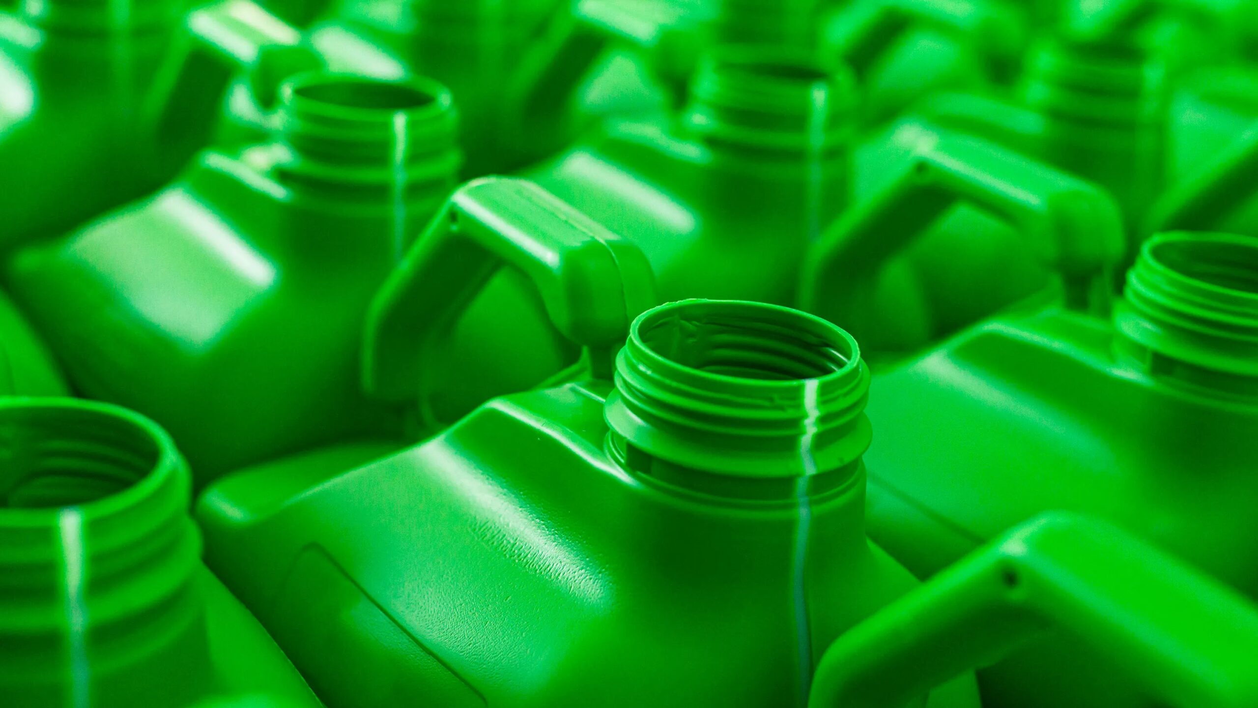 Ряд зеленых пластиковых канистр с ручками, крупный план. Экологичная тара для жидкости.