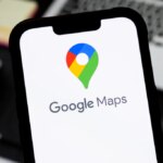 Смартфон с логотипом Google Maps на экране, фон с ноутбуком и блокнотом.