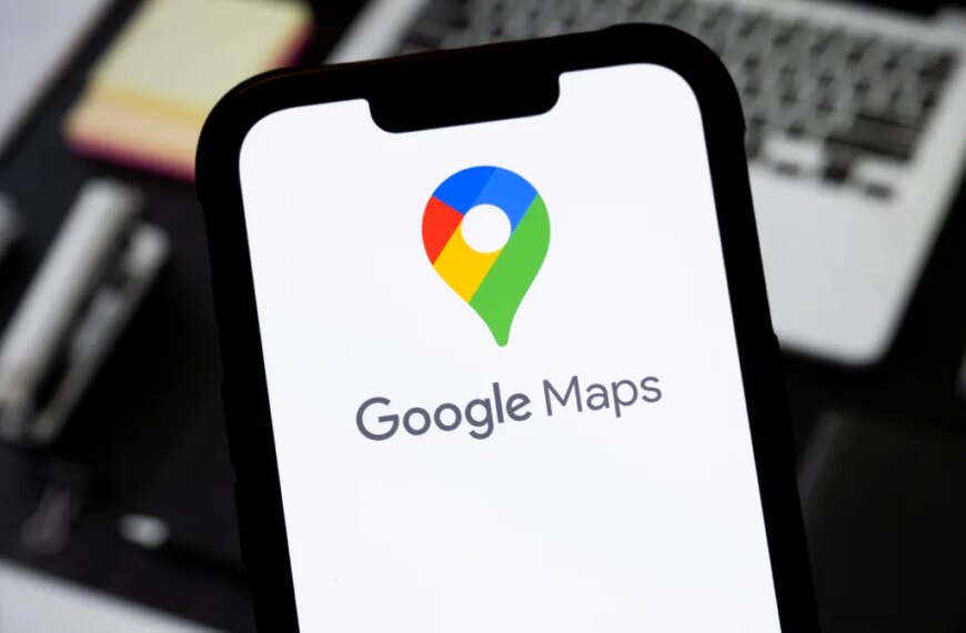 Смартфон с логотипом Google Maps на экране, фон с ноутбуком и блокнотом.
