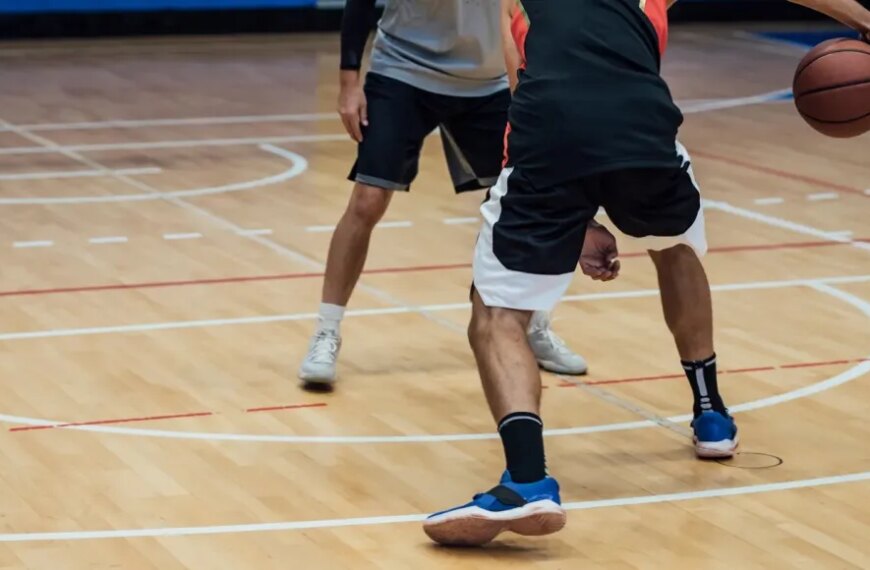 Баскетболисты играют в зале, один делает дриблинг.