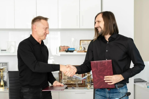 Два человека обмениваются рукопожатием в офисе, держа папки с документами.