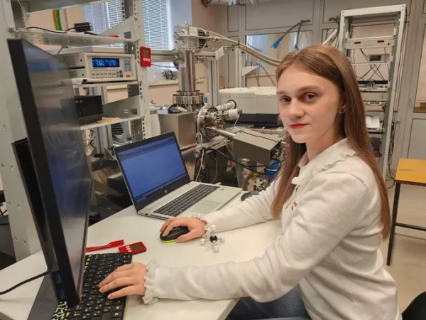 Исследователь в лаборатории перед компьютером, научное оборудование на заднем плане.