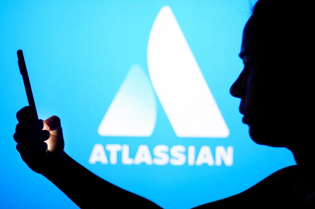 Силуэт человека с телефоном на фоне логотипа Atlassian.