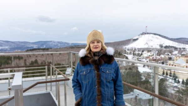 Человек в тёплой одежде на фоне зимнего горного пейзажа и смотровой площадки.