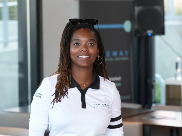 Женщина в белой рубашке с логотипом, улыбается в помещении.