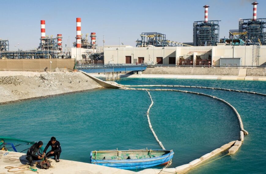 Промышленная станция на берегу синих вод с людьми на причале и лодкой.