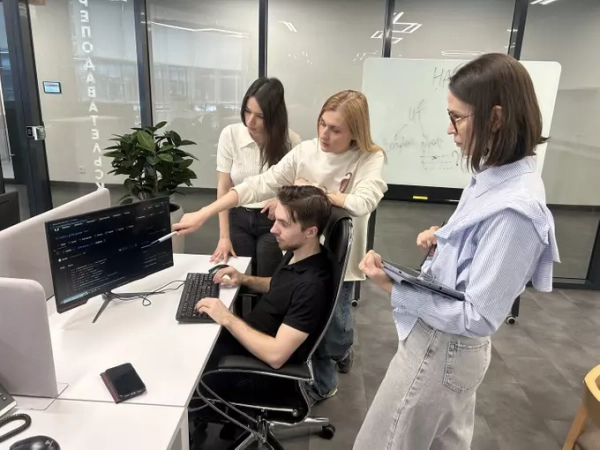 Коллектив сотрудников обсуждает программный код в офисе перед компьютером.