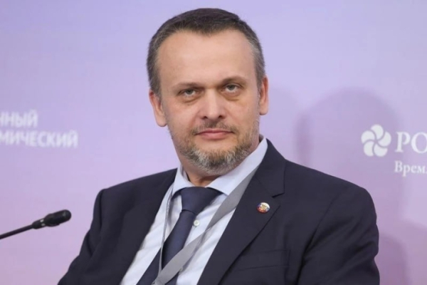 Мужчина в костюме на конференции, микрофон, фиолетовый фон, корпоративная атмосфера.