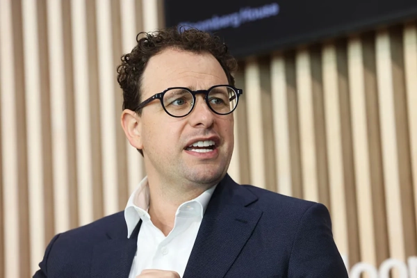 Мужчина в костюме выступает на конференции, микрофон в ухе. Рифленый фон.