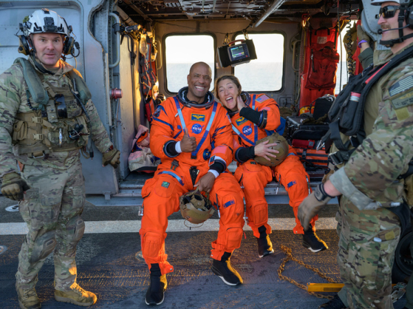 Астронавты в оранжевых скафандрах и военные на борту вертолёта, спасательная операция.