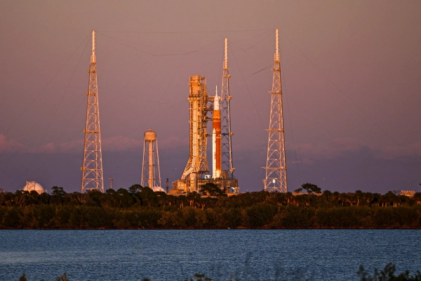 Ракета на стартовой площадке на фоне заката у воды.