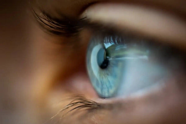 Голубой глаз человека вблизи, с длинными ресницами и отражением света в роговице.