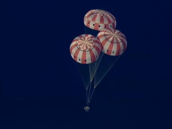 Капсула с тремя яркими парашютами в небе, безопасное приземление космического аппарата.