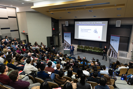 Лекция в аудитории университета, докладчики и слушатели, презентация на экране.