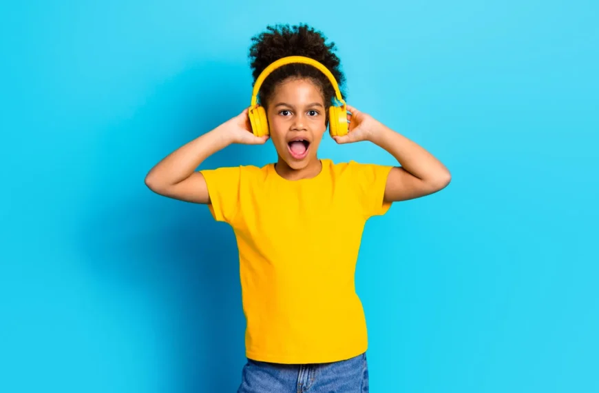 Ребёнок в жёлтых наушниках и футболке на голубом фоне, слушает музыку.