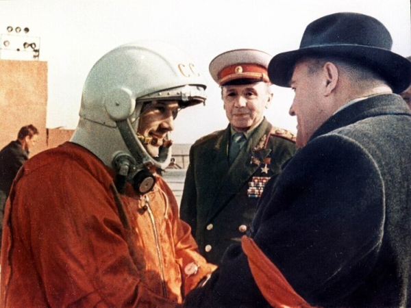 Советский космонавт в костюме приветствует людей, включая военного. Космонавтика СССР.