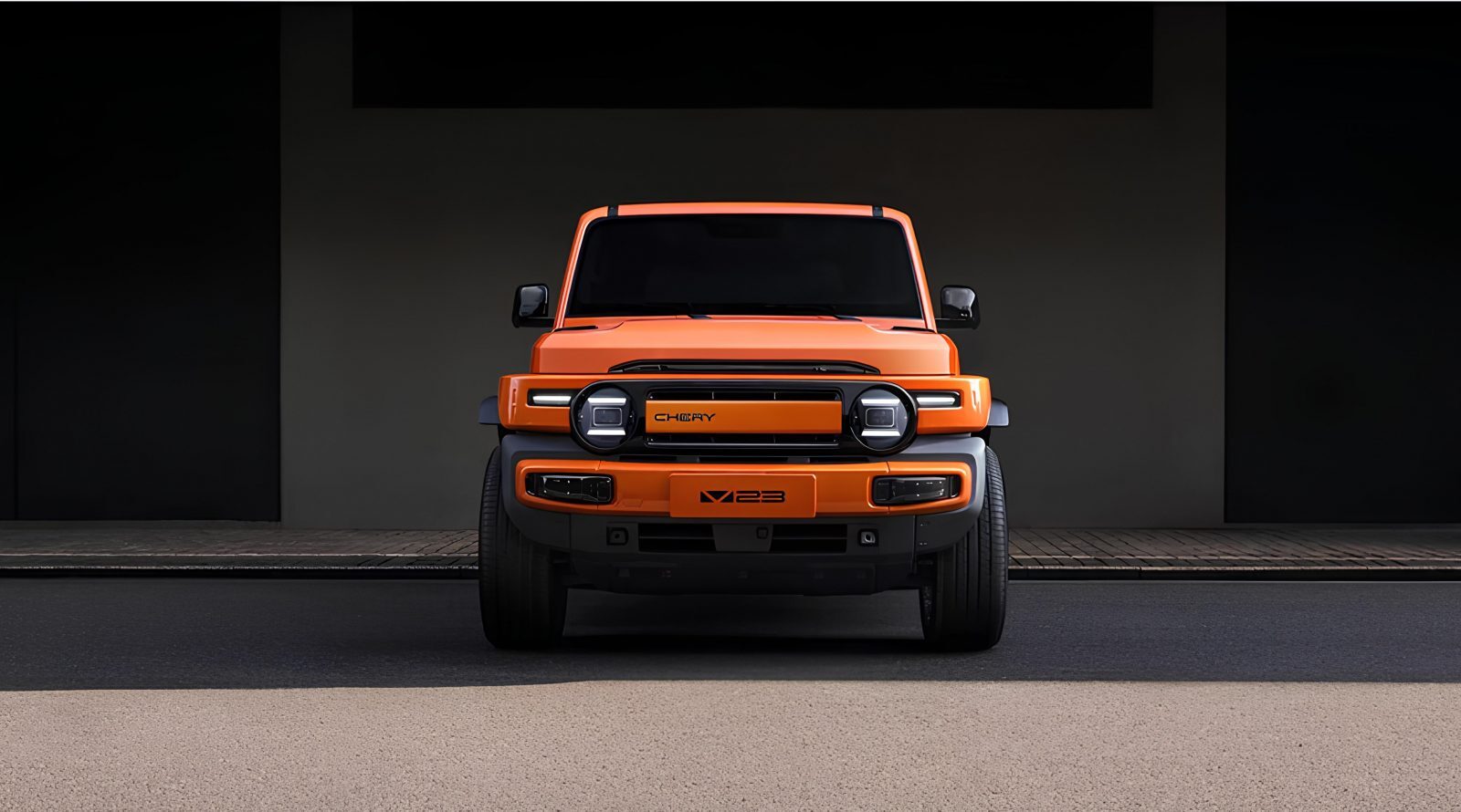 Оранжевый внедорожник Chery X23, вид спереди, на фоне бетонной стены.