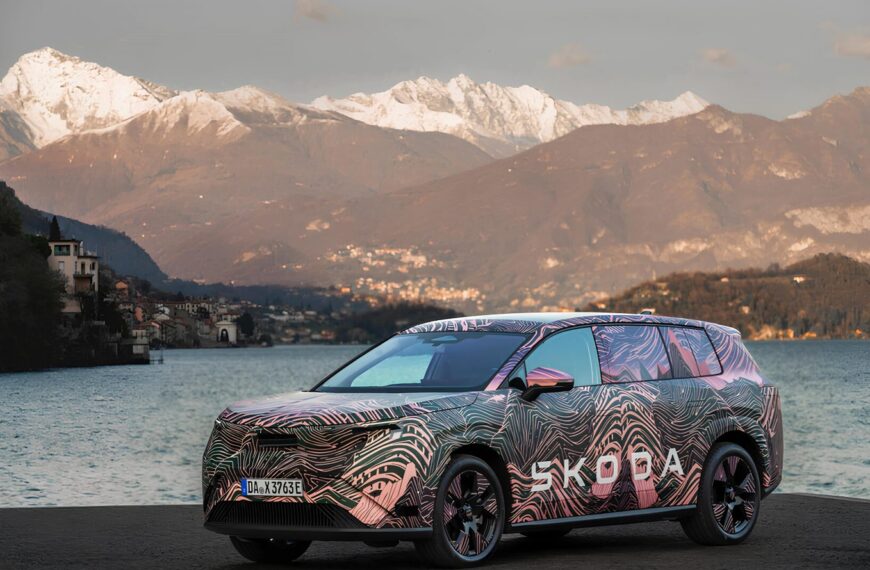 Автомобиль Skoda с камуфляжем на фоне горного озера и снежных вершин.