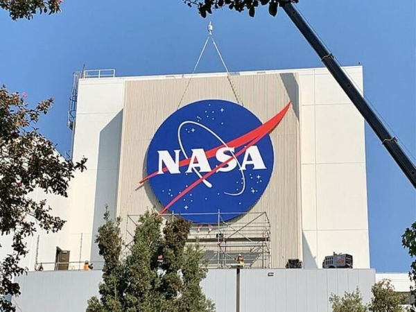 Логотип NASA на здании, окружённый строительными лесами и деревьями.