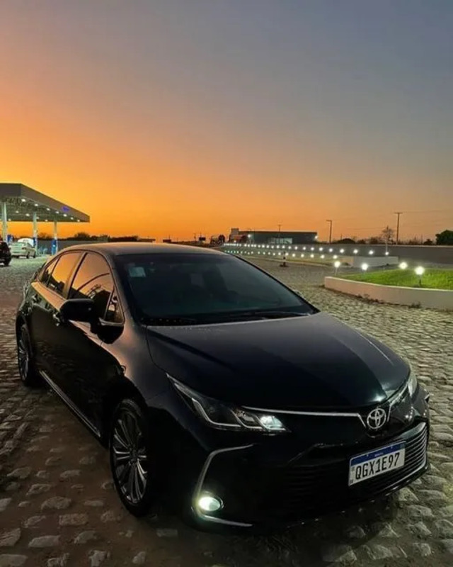 a black car parked in front of a gas station at night with the sun setting