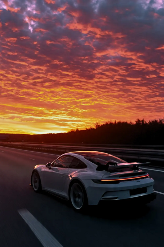 a white sports car driving down the road at sunset or dawn with clouds in the sky