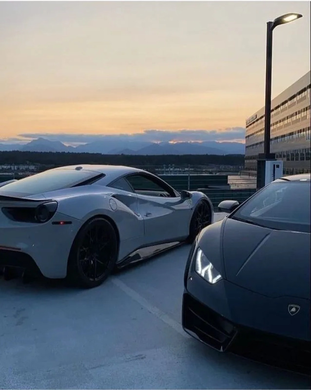 two sports cars parked next to each other in a parking lot at sunset or dawn