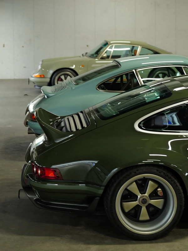 several cars are lined up in a parking garage, one is green and the other is black
