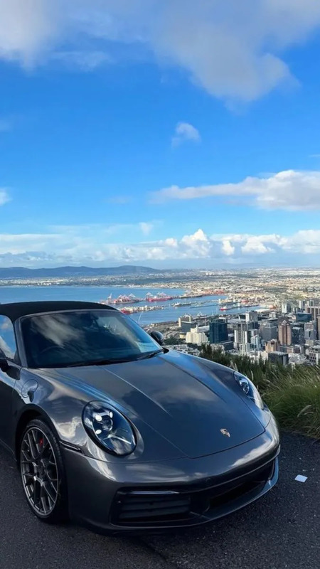 a grey sports car parked on the side of a road next to a large city