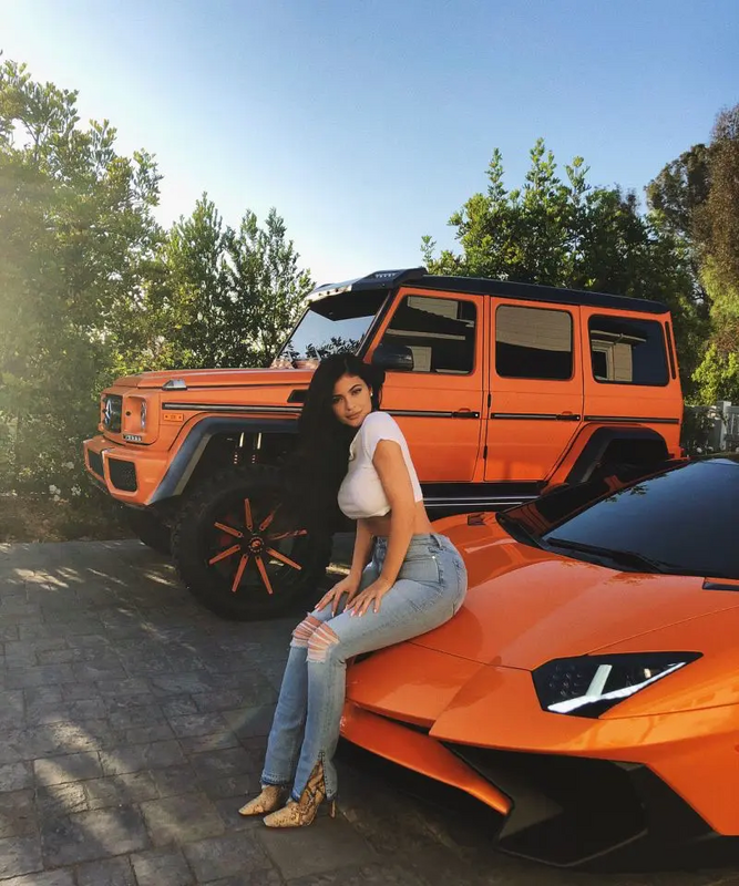 a woman sitting on top of an orange sports car