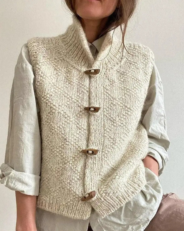 a woman wearing a white sweater with buttons on the front and sleeves, standing against a wall